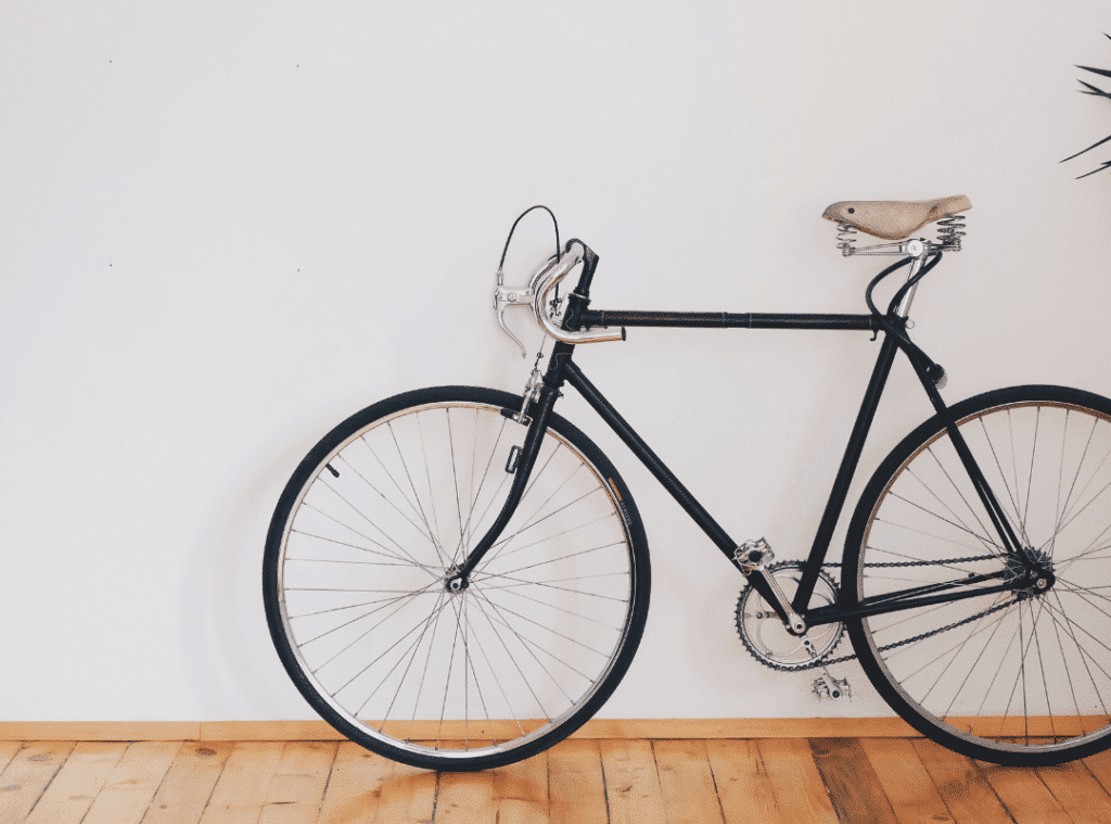 Vélo vintage noir appuyé sur un mur blanc avec sol en parquet