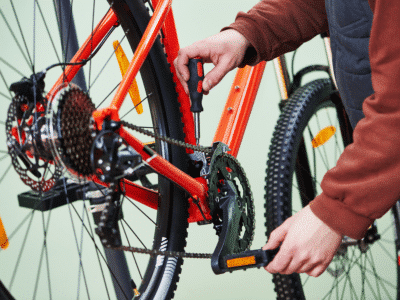 Zoom sur le pédalier d'un vélo. Des mains d'homme font tourner la manivelle et réparent la chaîne.