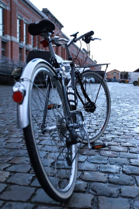 Tout savoir sur le moteur ANNAD 4 Vélo de ville vintage chromé posé sur la béquille au milieu d'une route pavée. Equipé à l'avant d'un moteur discret et d'un écran de contrôle en Bluetooth.