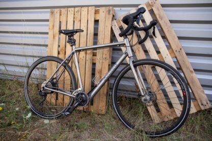 Vélo Gravel Annad en titane sur fond bois équipé d'un kit d'électrification composé d'un moteur avec batterie interne placé dans le moyeu de la roue arrière