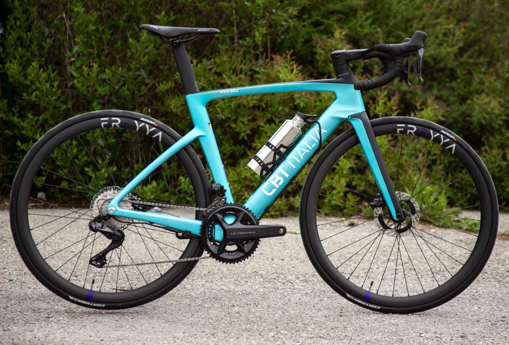 Paire de jantes carbone haut de gamme FREYYA installée sur CBT Mystero bleu. Le vélo est au premier plan sur un chemin de graviers avec arbres en arrière plan.